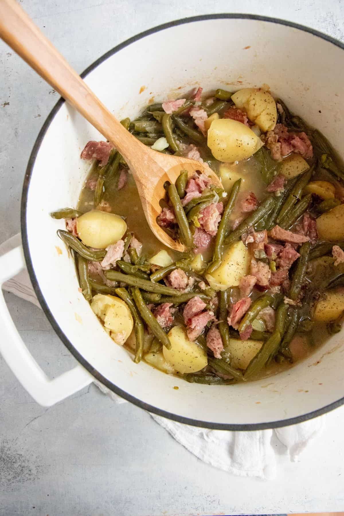 Southern Style Green Beans and Potatoes in a white Dutch oven, with a wooden spoon