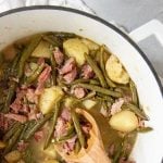 Southern Style Green Beans and Potatoes in a white Dutch oven, with a wooden spoon, with a text overlay
