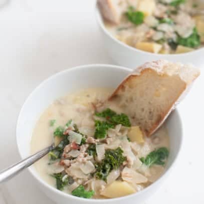 Two bowls of soup with spoons and pieces of bread dunked inside.
