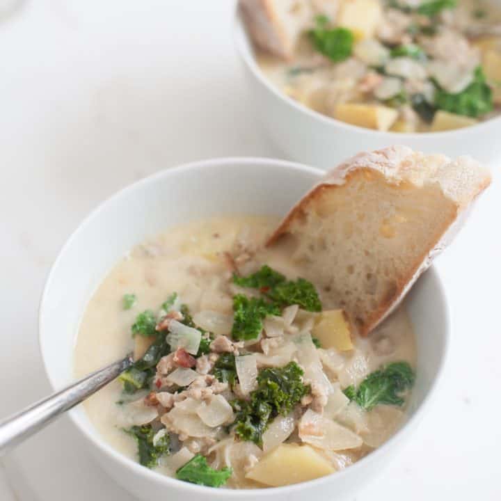 Two bowls of soup with spoons and pieces of bread dunked inside.