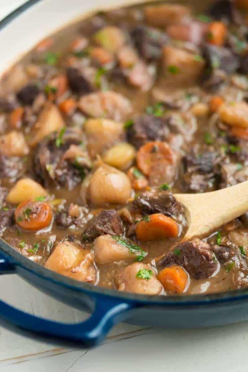 A wooden spoon dips into a pot of beef stew with red wine.