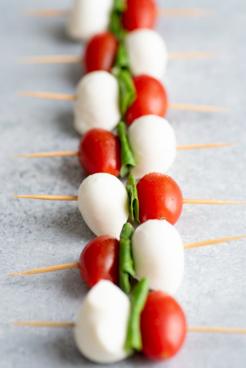 Side angle shot of Caprese Sticks lined up on a grey background