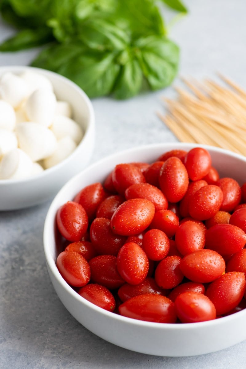 Side angle shot of Caprese Sticks ingredients - cherry tomatoes, mozzarella balls, basil, and toothpicks