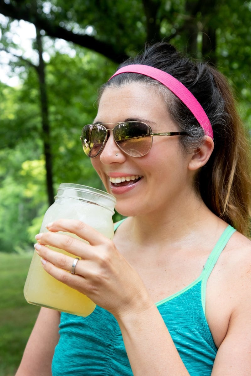 Woman in a turquoise sports bra smiling and drinking a glass jar of Homemade All-Natural Electrolyte Drink