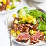 Blackened tuna steak topped with mango avocado salsa on a plate, cut to show the perfectly cooked pink interior.