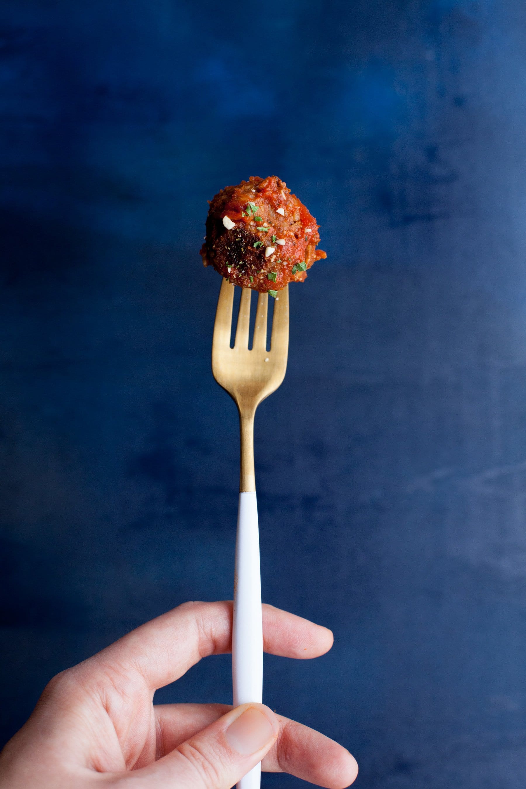 Hand holding a white-handled fork with a vegan meatball skewered on it.