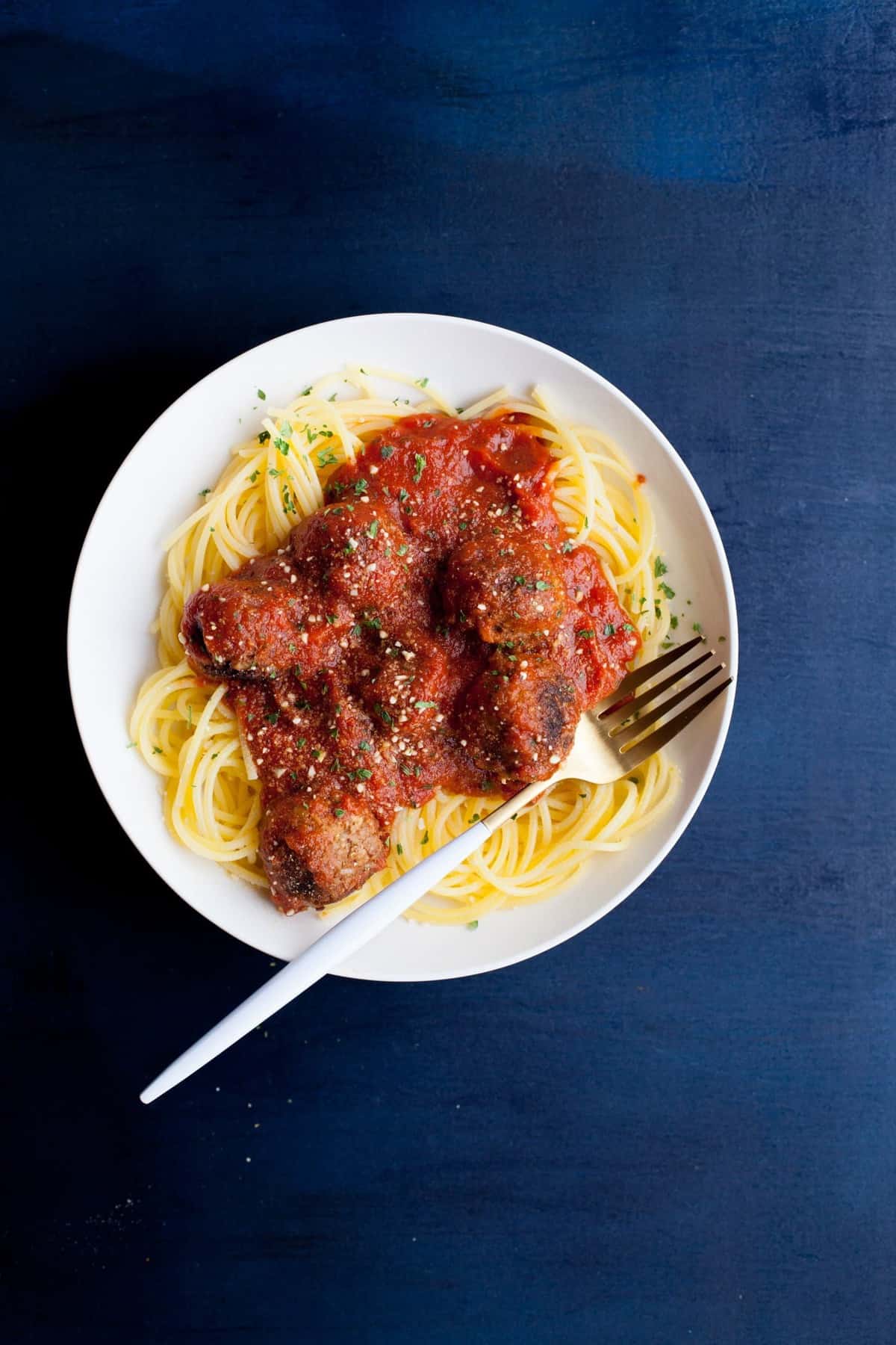 White plate filled with spaghetti, vegan meatballs, and marinara sauce on a blue background.