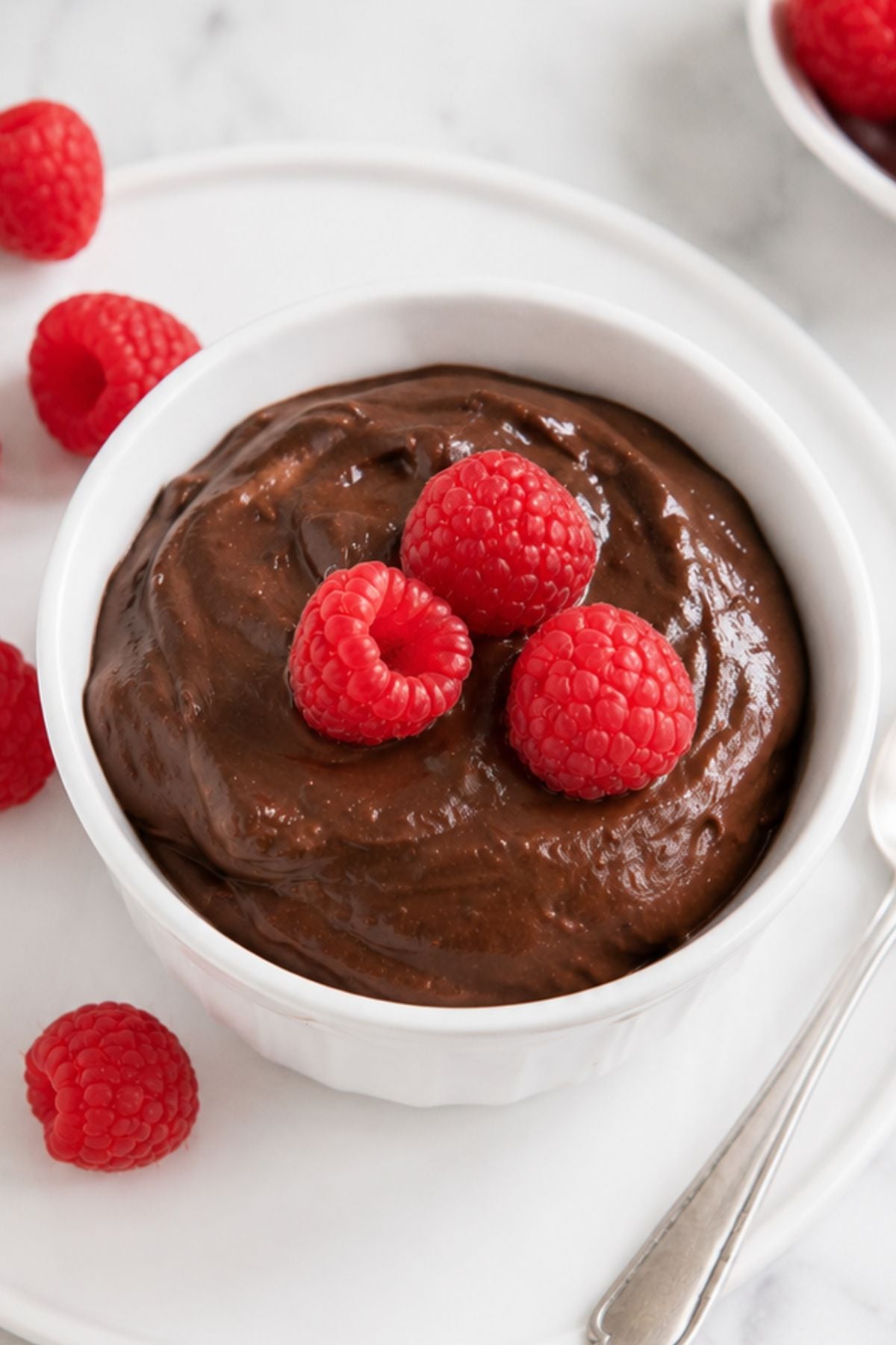 Creamy avocado pudding in a white ramekin, garnished with three fresh raspberries.