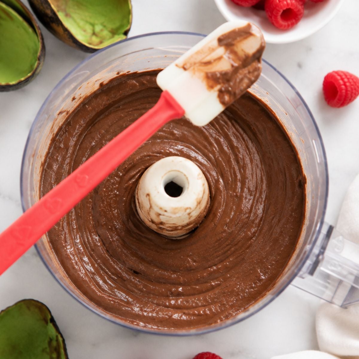 Freshly blended avocado chocolate mousse in a food processor, smooth and glossy, with a spatula resting on top.