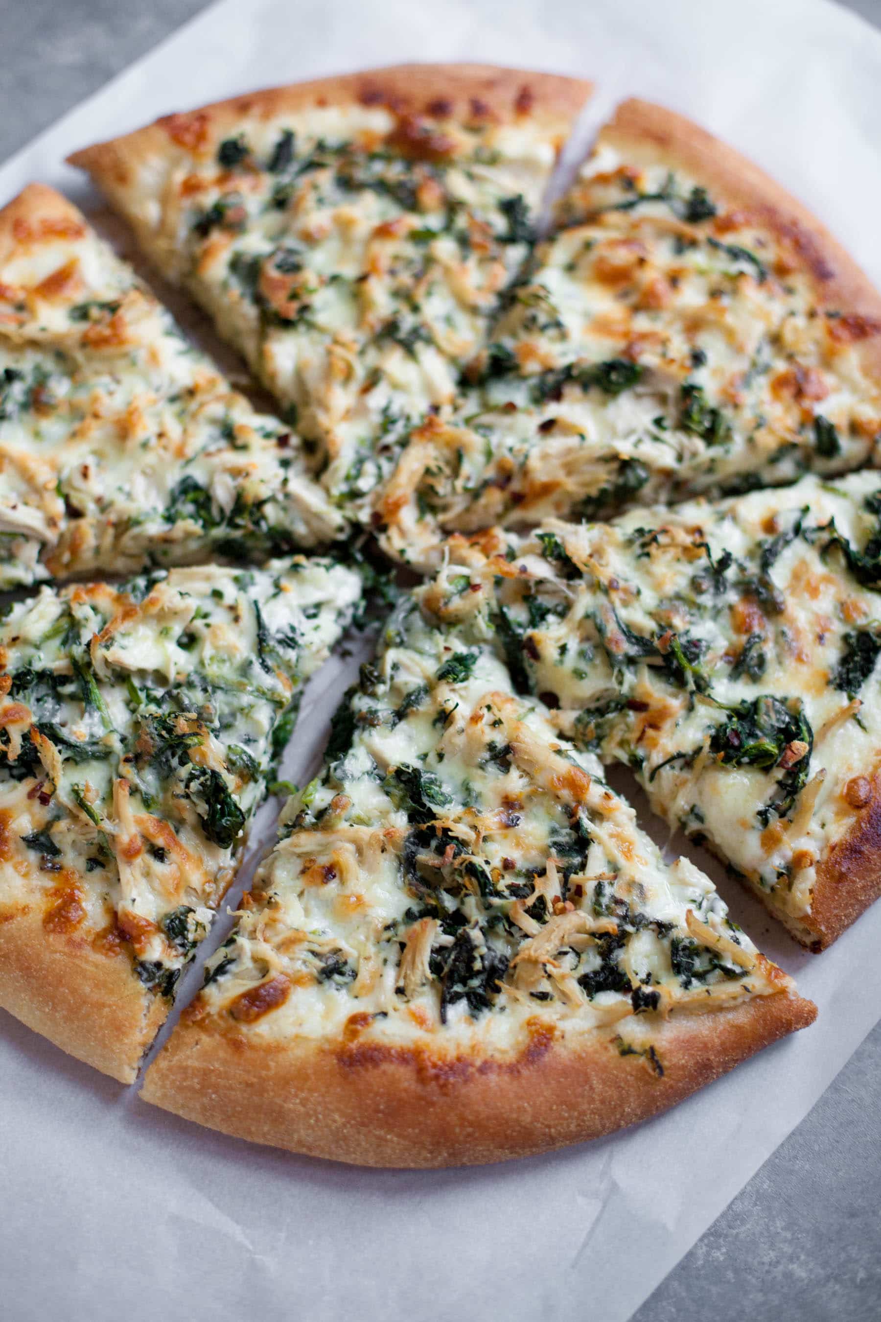 Chicken Spinach Alfredo Pizza, cut into slices on a white background.