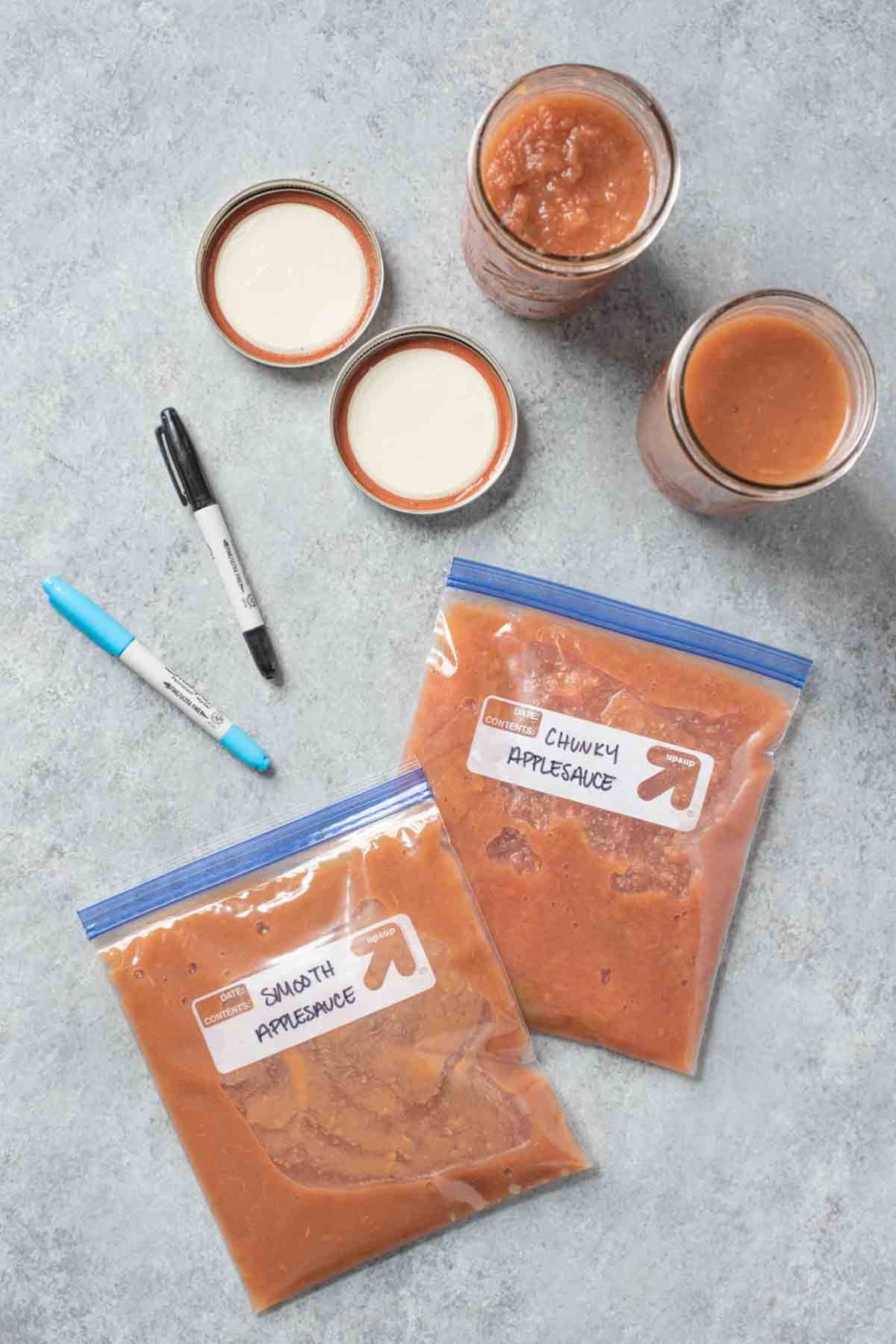 Freezer bags of applesauce and jars of applesauce sit on a countertop ready to go in the freezer