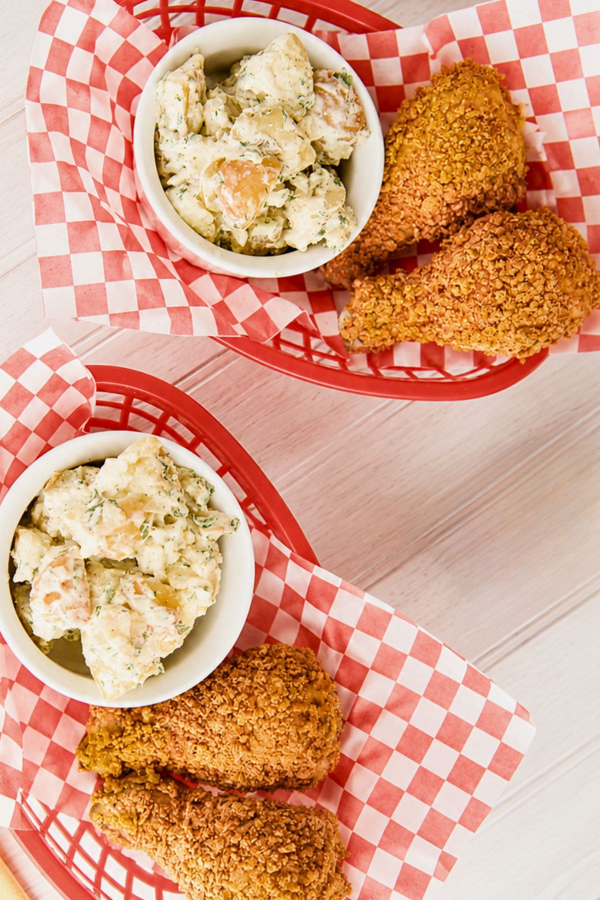 Two baskets of baked fried chicken legs served with potato salad