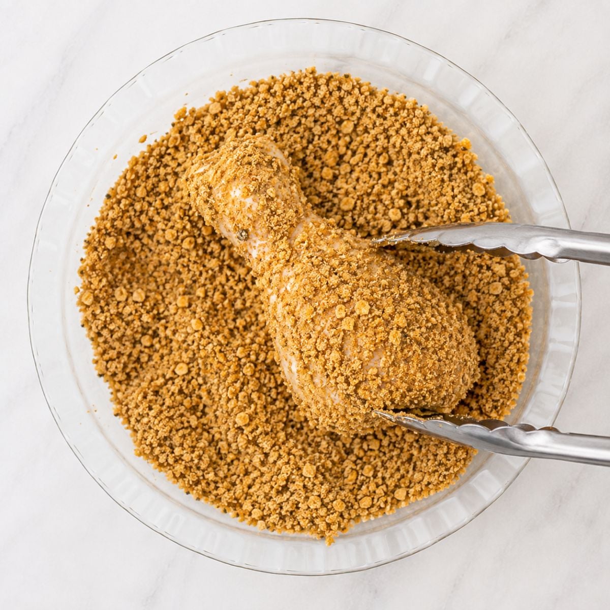 Chicken drumstick being coated in crushed cornflake crumbs