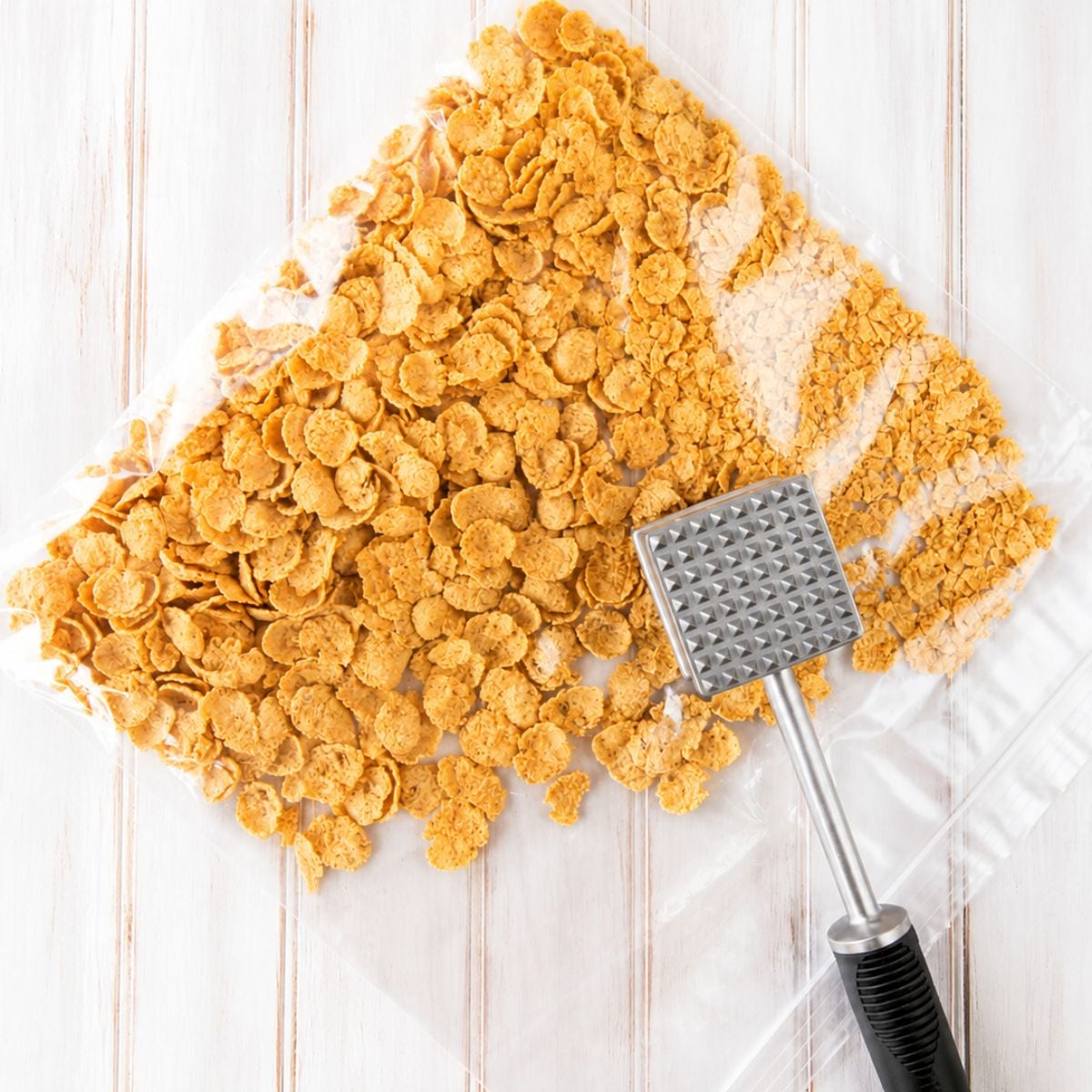 Crushed cornflakes in a plastic bag being crumbled with a meat mallet