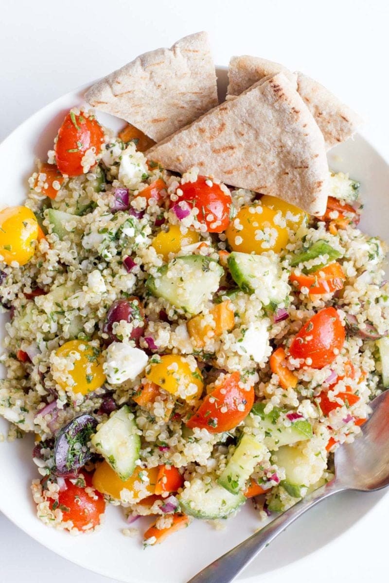 Greek Quinoa Salad in a white bowl, with triangles of pita bread on the side