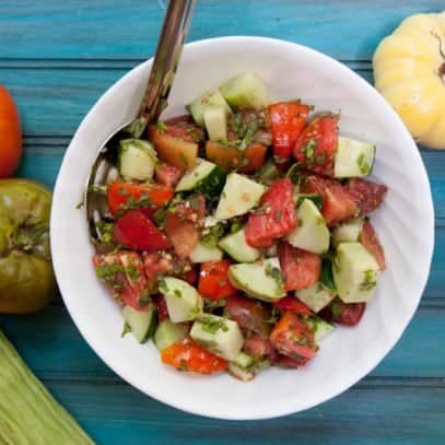 Cucumber tomato salad in a white bowl on a teal backdrop