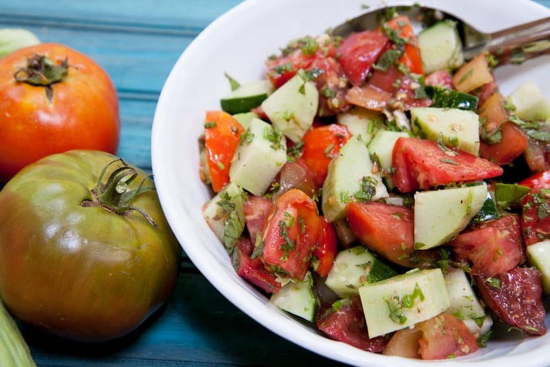 Cucumber, tomatoes, and herbs tossed in a simple vinaigrette in a white bowl