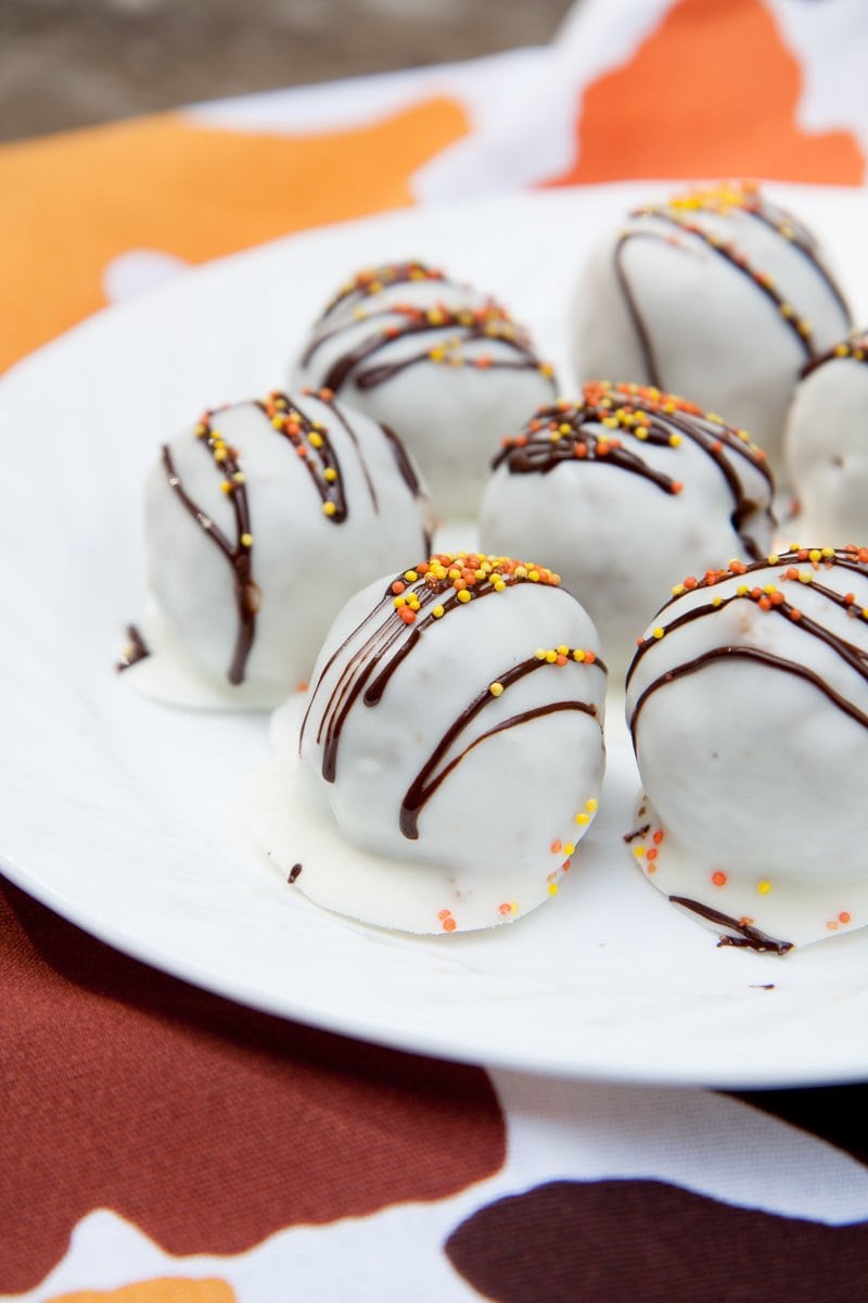 Cake balls coated in white and drizzled with chocolate and orange sprinkles on a white plate.