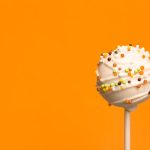 A cake pop covered with white candy melt and Halloween sprinkles.