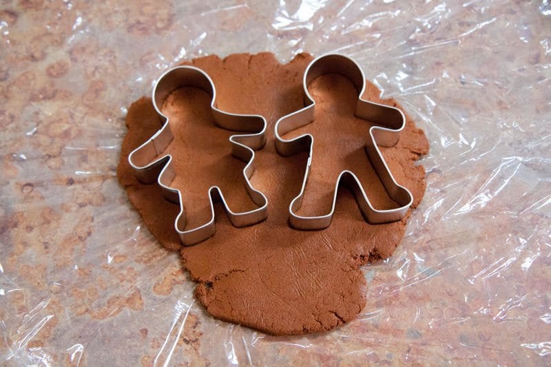 Two person-shaped cookie cutters sit on top of rolled out dough.