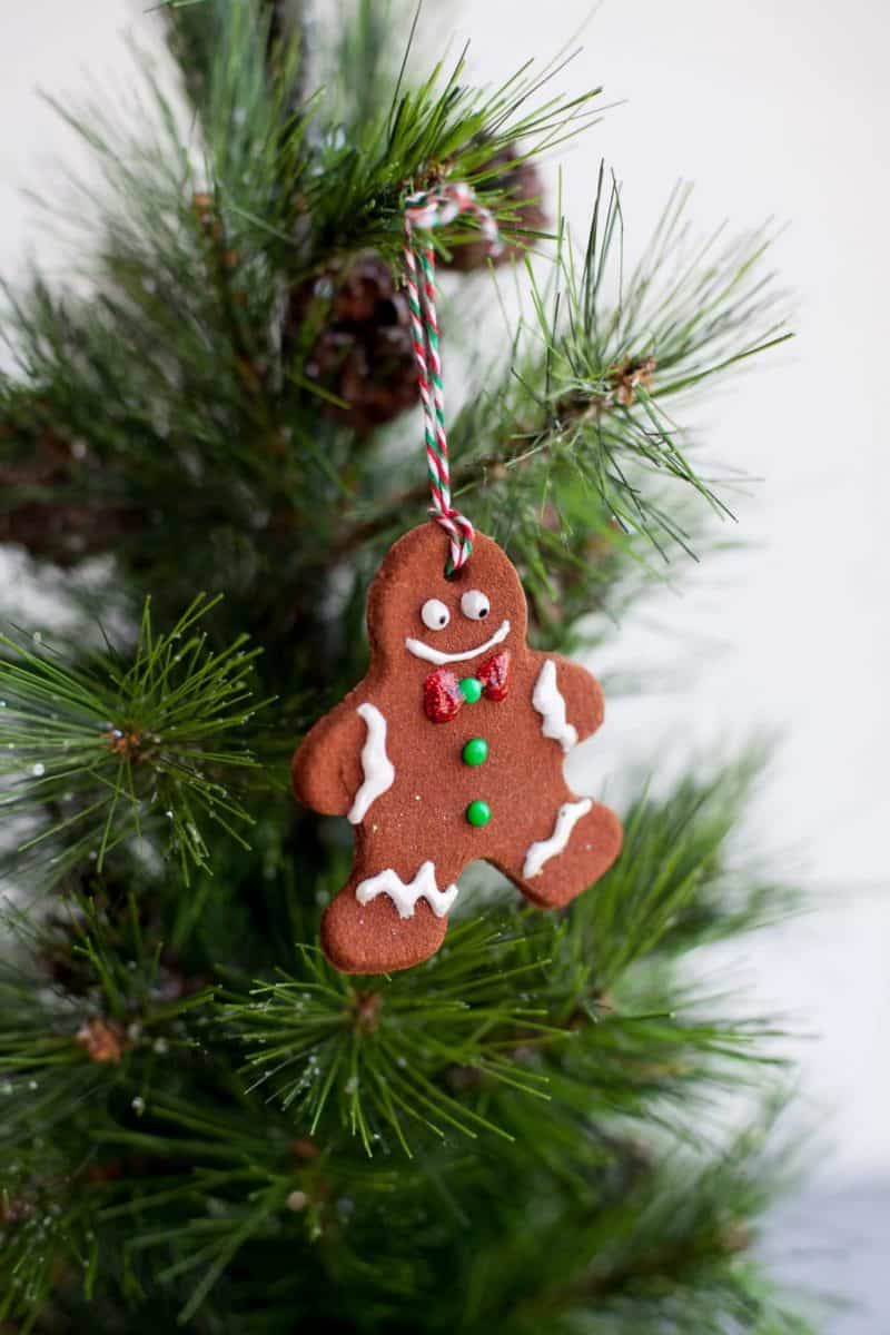 A cinnamon ornament shaped and decorated like a gingerbread person hangs from a evergreen tree.
