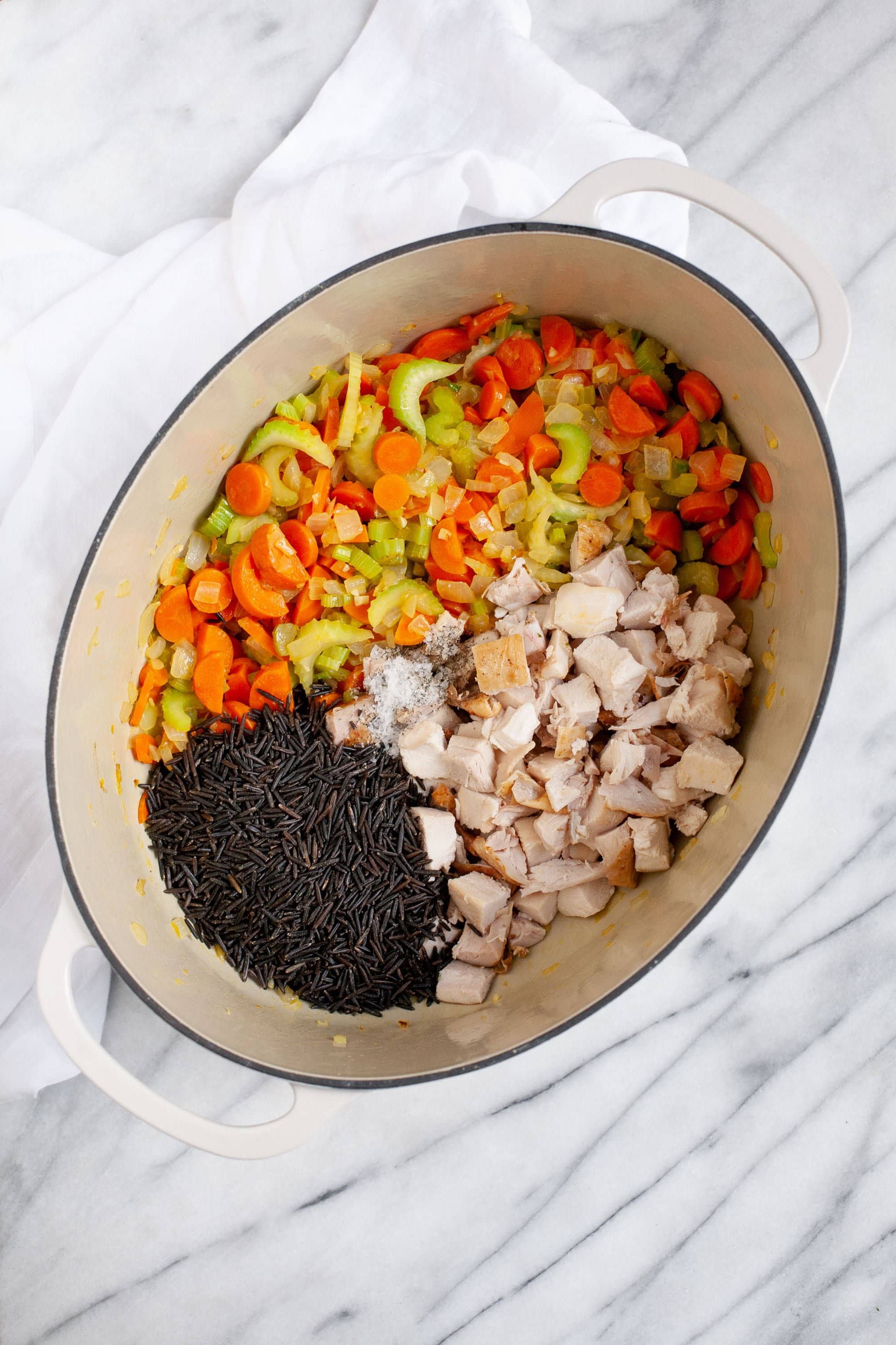 Ingredients in a Dutch oven, including wild rice, chopped vegetables, and chopped poultry