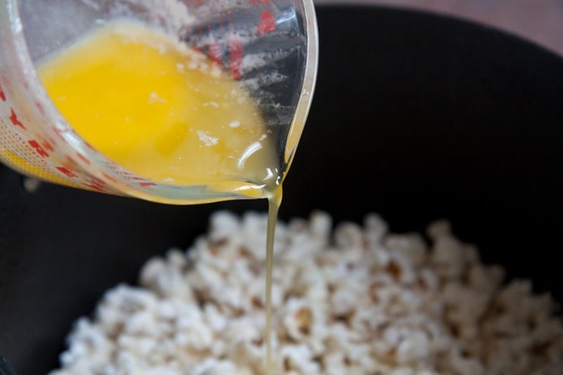 Melted butter pours into freshly popped Movie Theater Popcorn.