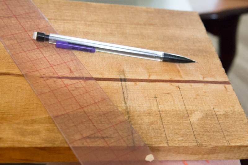 Mechanical pencil and a ruler resting on top of a wooden board, marking ruler ticks.