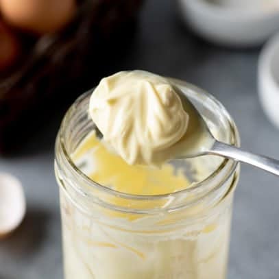Side-angle shot of Homemade Mayo getting spooned out of a glass jar