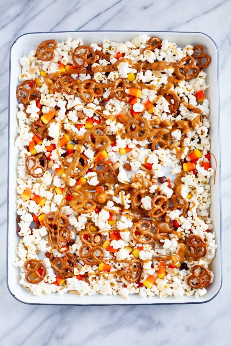 Overhead of popcorn on a sheet pan with pretzels, candy corn, Reese's Pieces, and a peanut butter caramel sauce drizzle.
