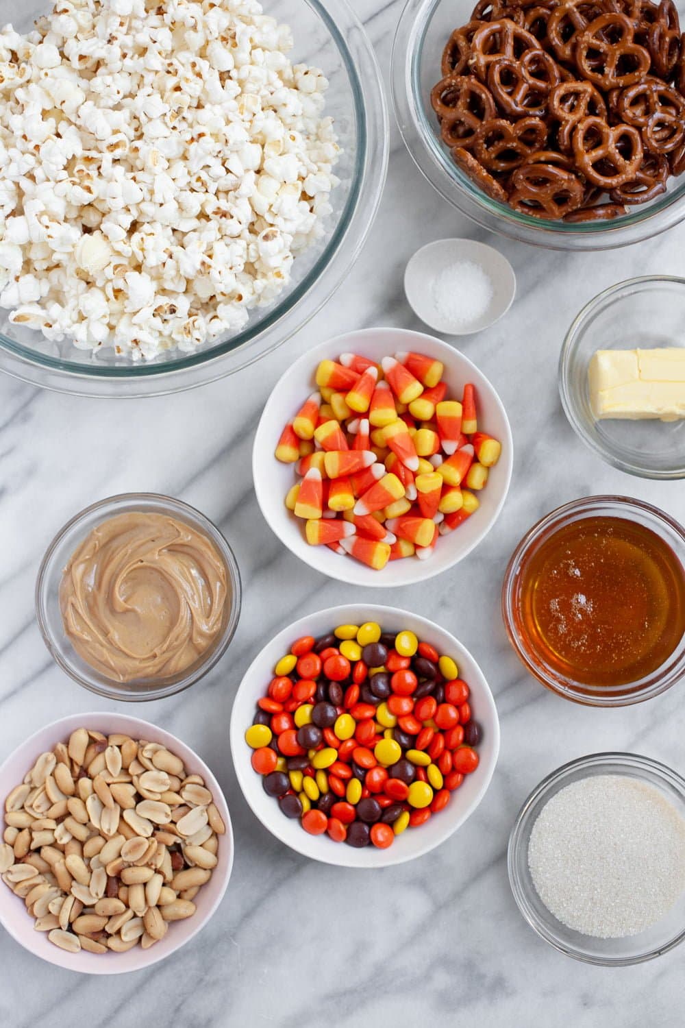 Ingredients for Peanut Butter Monster Munch Halloween Party Mix in individual bowls - popcorn, peanut butter, Reese's Pieces, candy corn