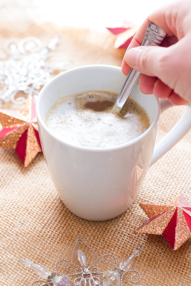A hand holding a spoon stirs a homemade gingerbread latte.