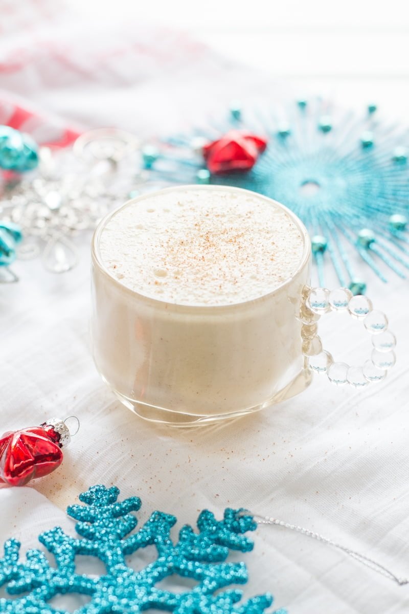 Glass of Coconut Milk Eggnog surrounded by blue and red holiday decorations.
