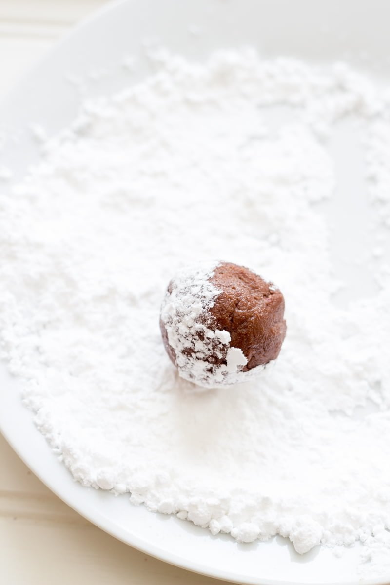 A chocolate dough ball in a shallow plate of powdered sugar