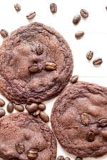 Three chocolate espresso cookies on a white background surrounded by espresso beans.