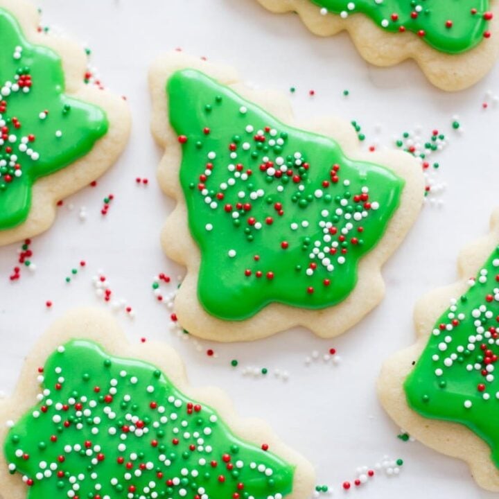 Decorated Christmas tree sugar cookies with green frosting and sprinkles rest on a white background.