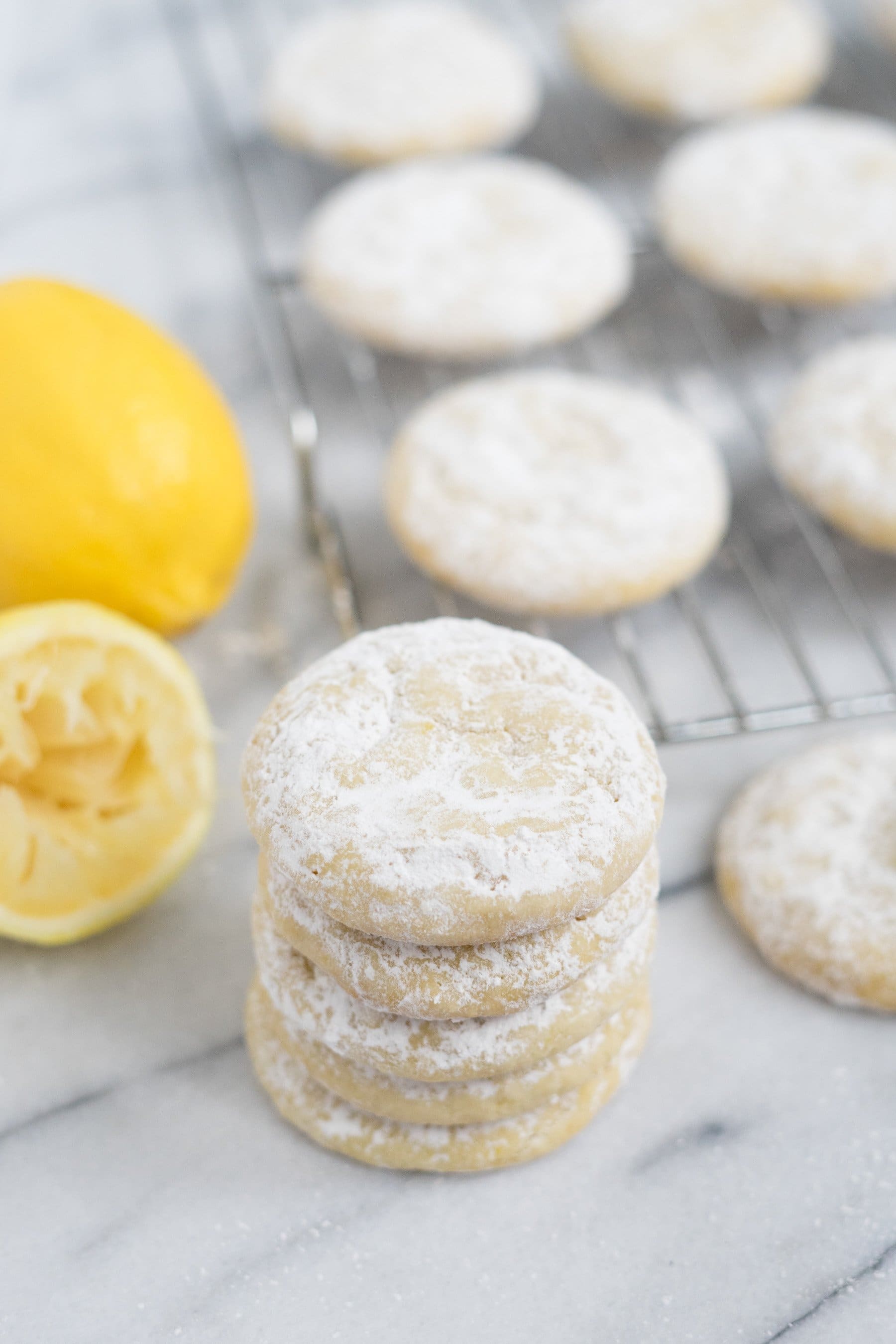 Stack of baked lemon cookies in front of a wire rack of cooling cookies