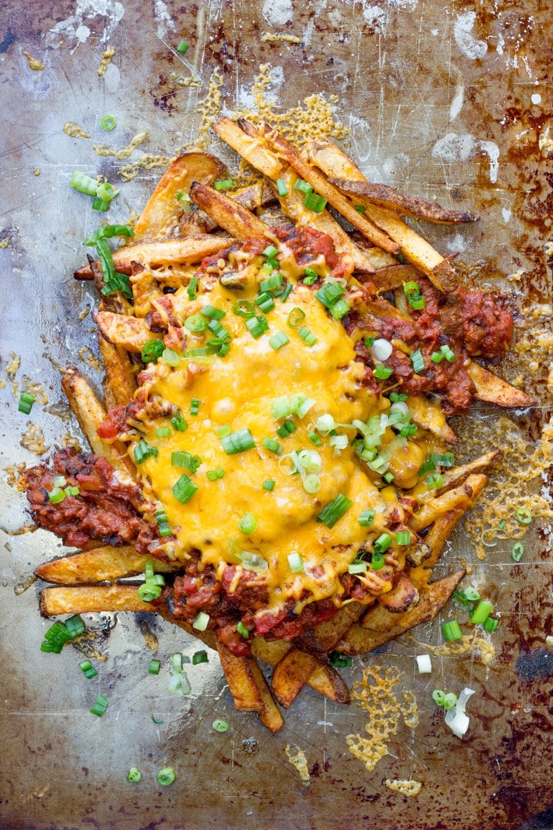 Oven baked fries on a baking sheet topped with homemade chili, melted cheese, and fresh green onions.