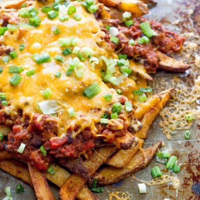 Oven baked fries piled high on a baking sheet, topped with homemade chili, melted cheddar cheese, and garnished with green onion.