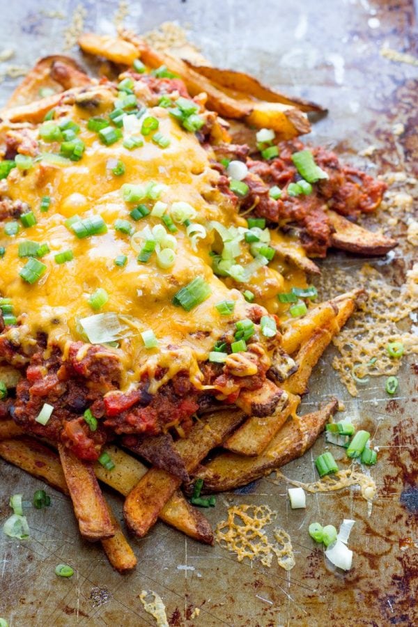 Oven baked fries piled high on a baking sheet, topped with homemade chili, melted cheddar cheese, and garnished with green onion.