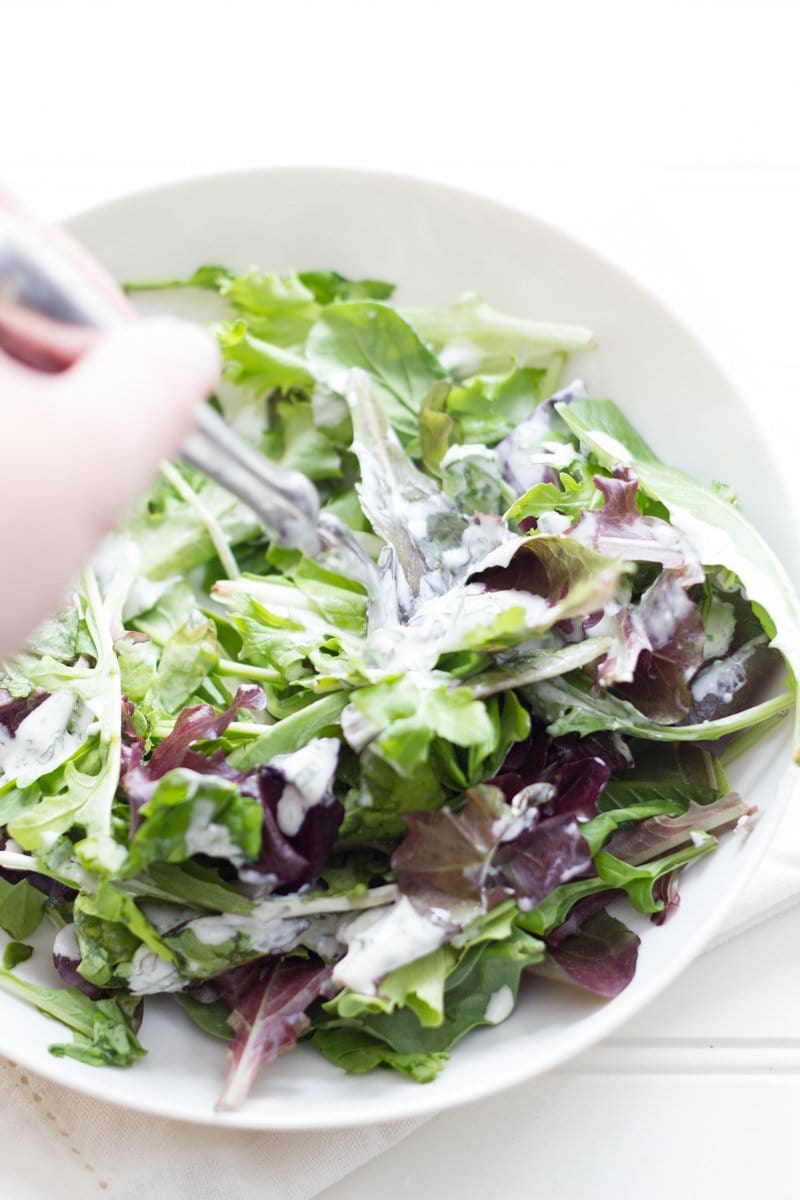 A hand holding a fork spears salad greens in ranch dressing.