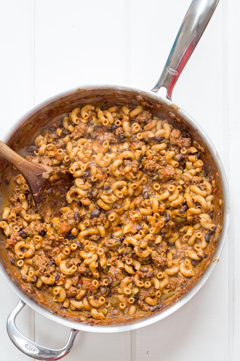 A pot of taco pasta skillet with a wooden spoon stirring it.