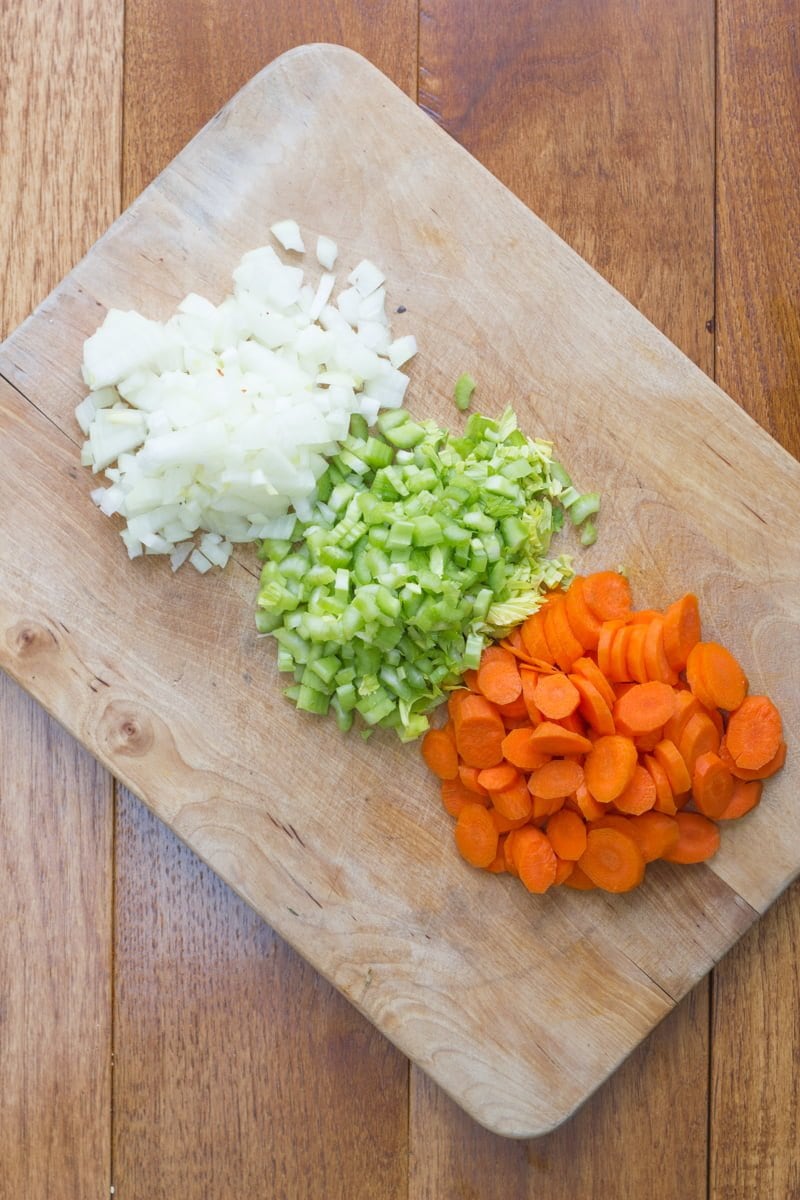Chopped onion, diced celery, and sliced carrot on a cutting board.
