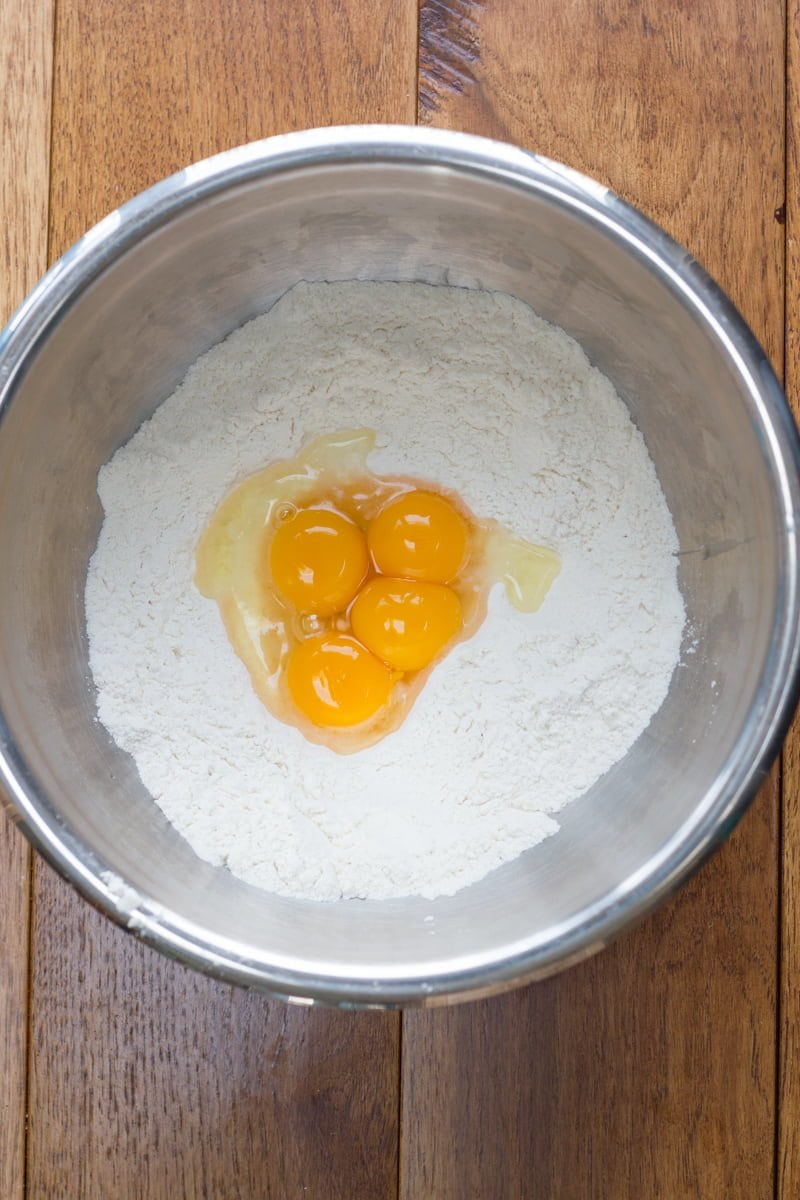 Overhead of flour in a bowl with egg yolks in a well in the center.