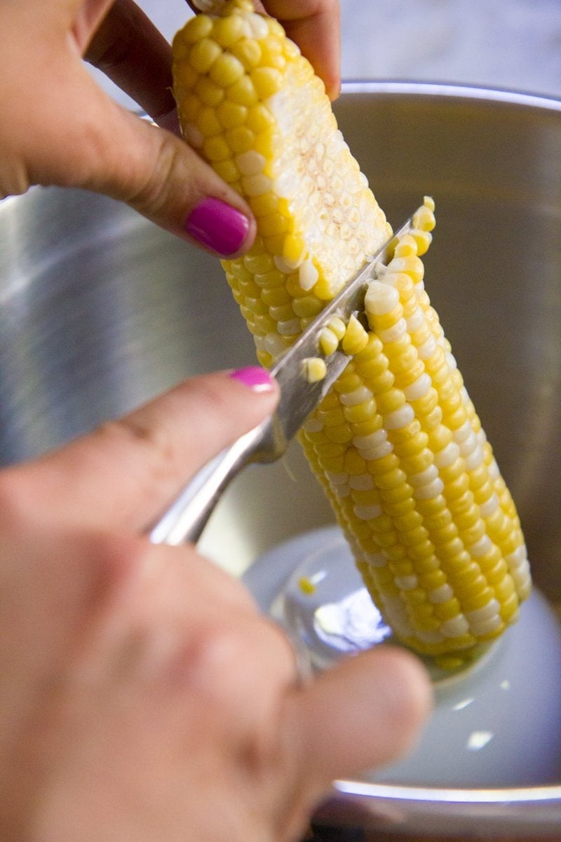 Close-up of cutting corn kernels from the cob by resting the cob on an overturned bowl inside a larger bowl.