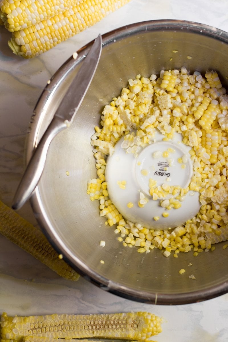 A large metal bowl with a smaller bowl turned upside-down inside it. The corn cob rests on the small bowl while the big bowl catches the kernels that are cut from the cob.