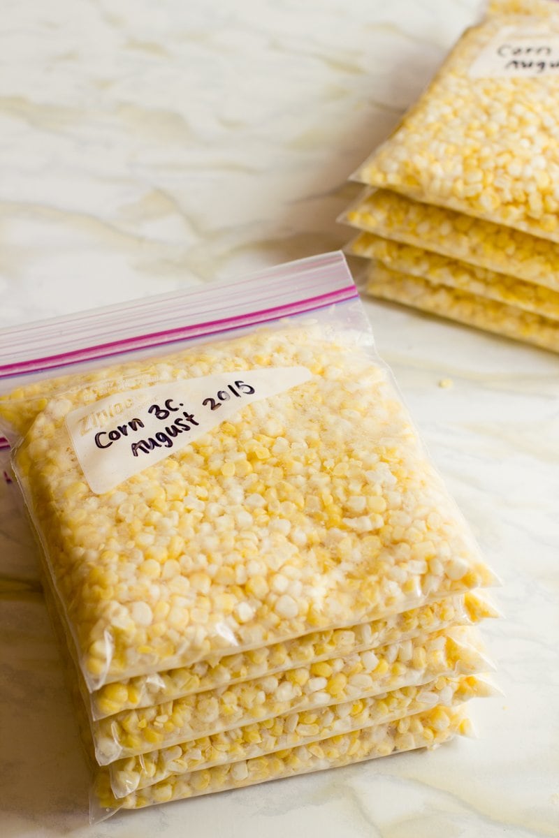 Five zip-top bags filled with 3 cups of fresh corn kernels labeled and stacked on a countertop.