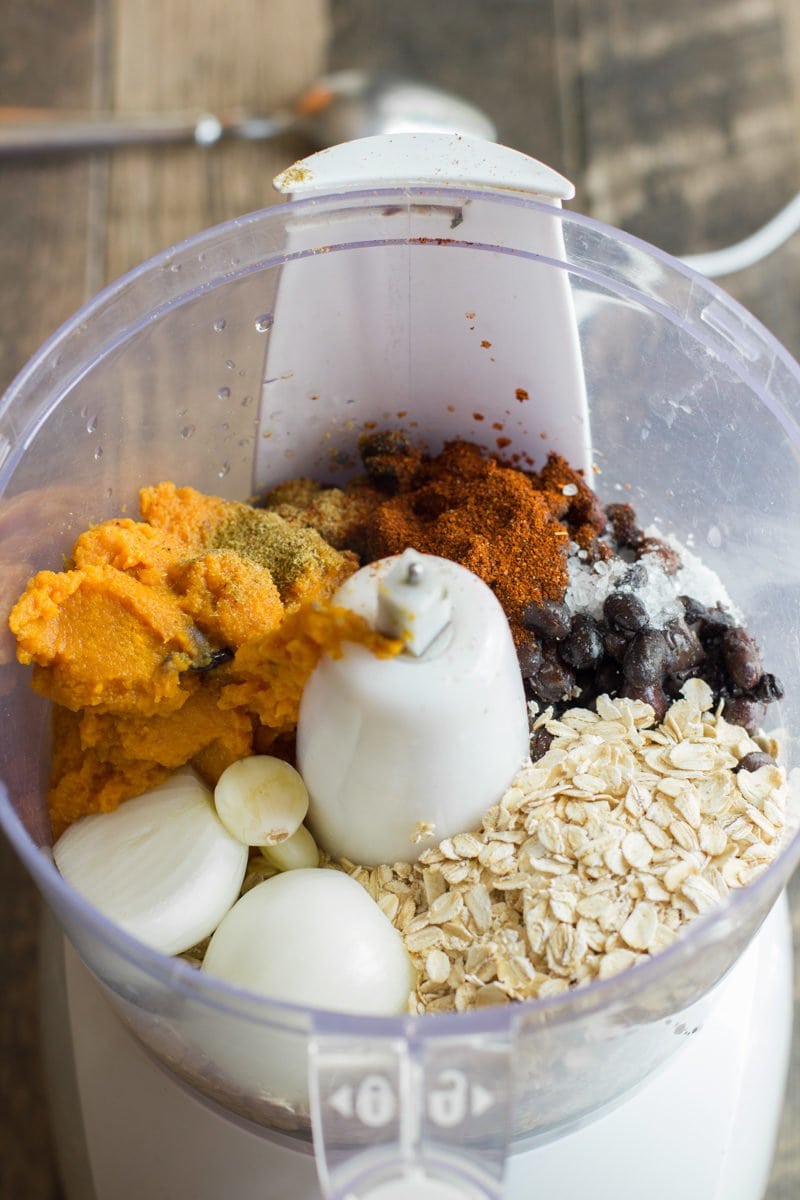 Ingredients to make burgers sits in a food processor - oatmeal, sweet potato, onion, seasonings and sweet potatoes.