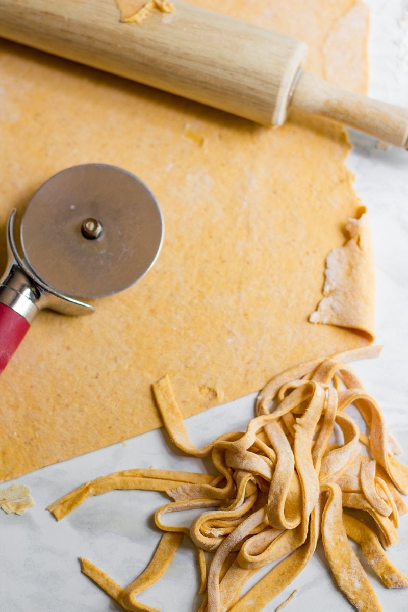 Pasta dough rolled onto a counter and cut into strands with a pizza cutter.