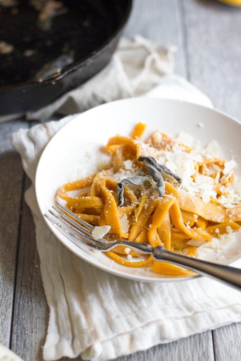 Pumpkin pasta served on a white plate and garnished with cheese and sage.